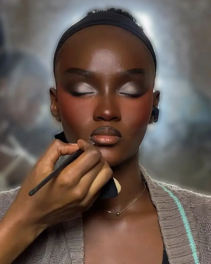 Dimma’s brush on a client’s cheek: deep brown skin, closed eyes, bronze lids and a nude lip